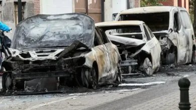 سيارات محترقة ومتضررة بالكامل متوقفة على جانب شارع مع آثار الحريق والحطام حولها