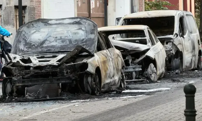 سيارات محترقة ومتضررة بالكامل متوقفة على جانب شارع مع آثار الحريق والحطام حولها