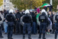 عناصر من الشرطة البلجيكية بملابس مكافحة الشغب يقفون أمام مجموعة من المتظاهرين في أحد الشوارع