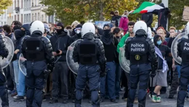 عناصر من الشرطة البلجيكية بملابس مكافحة الشغب يقفون أمام مجموعة من المتظاهرين في أحد الشوارع
