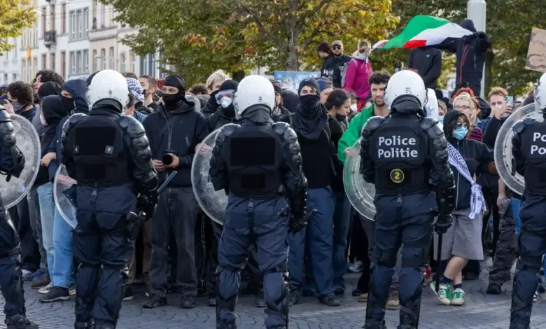 عناصر من الشرطة البلجيكية بملابس مكافحة الشغب يقفون أمام مجموعة من المتظاهرين في أحد الشوارع