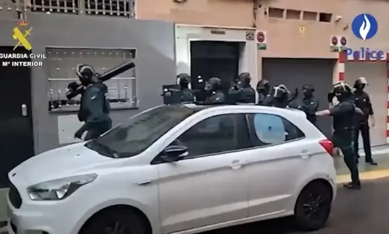 عناصر مسلحة من الحرس المدني الإسباني أمام مبنى خلال عملية أمنية مع سيارة بيضاء في المقدمة