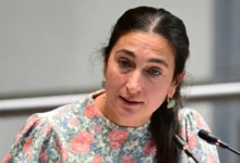 امرأة ترتدي ملابس مزينة بالورود وتتحدث أمام ميكروفونين خلال اجتماع رسمي