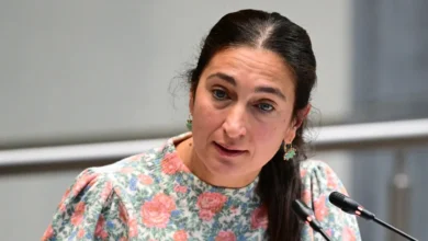 امرأة ترتدي ملابس مزينة بالورود وتتحدث أمام ميكروفونين خلال اجتماع رسمي