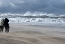 شخصان يحتميان من الرياح القوية على شاطئ وسط أمواج البحر الهائجة والغيوم الداكنة